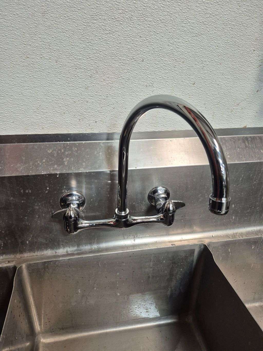 Finished wall-mounted faucet above an existing stainless-steel commercial sink in Spring Valley.